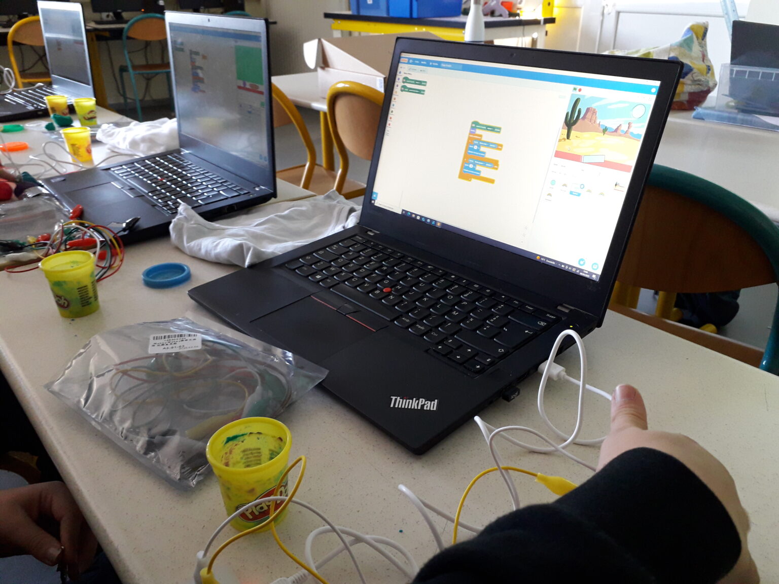 Ordinateur portable affichant un programme Scratch, entouré de matériel Makey Makey utilisé par un groupe d'élèves