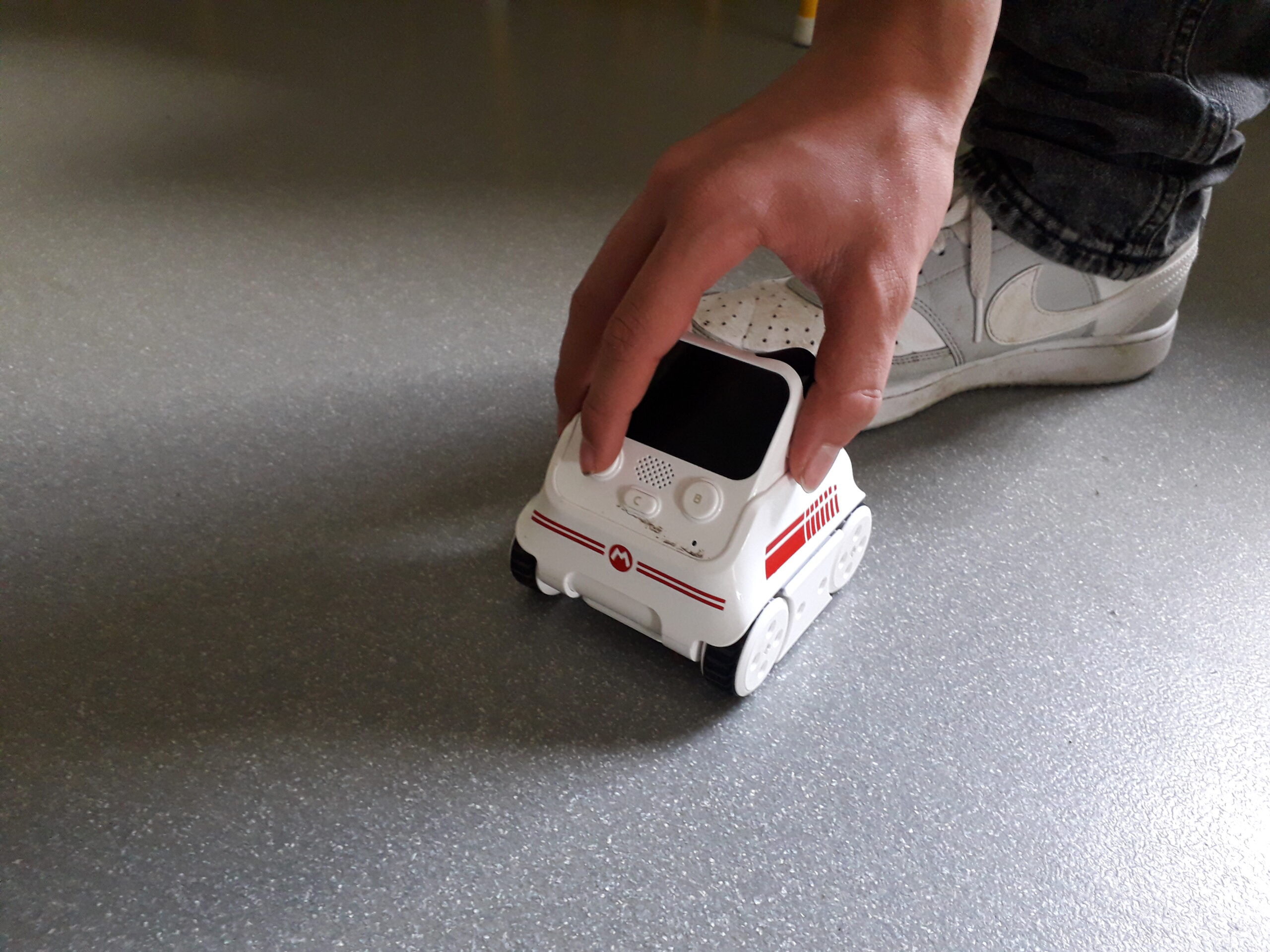 Main d'un enfant jouant avec un robot Codey Rocky au sol d'un atelier du Club Maker